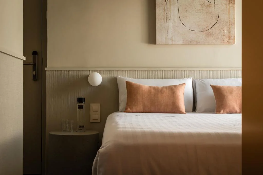 Habitación de hotel con la cama hecha y cojines en tonos teja