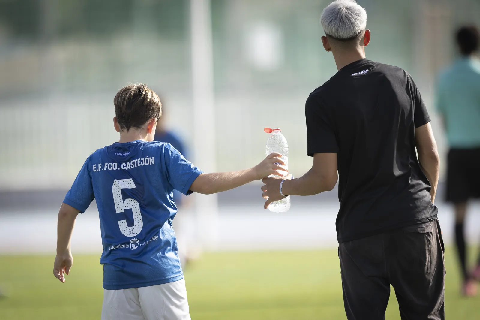 Un jugador y su entrenador, de espaldas, con una botella de agua en el torneo de fútbol base de Estepona