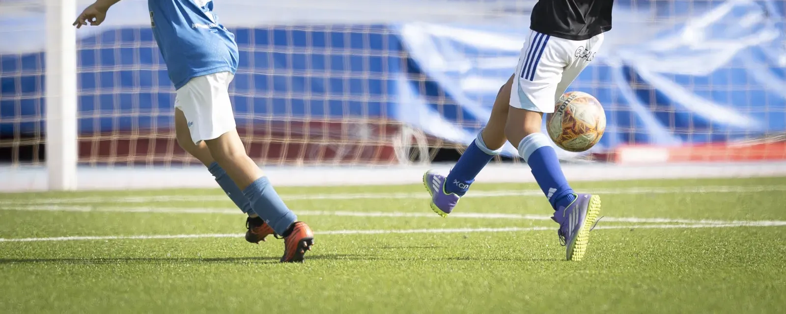 Piernas de dos jugadores y el balón delante de la portería